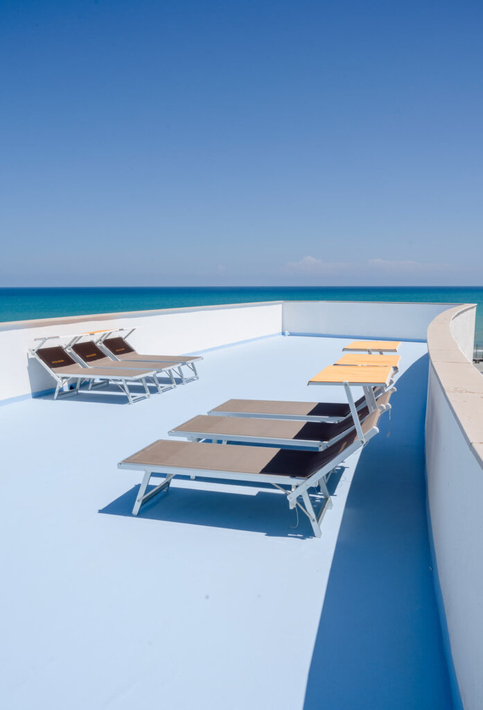 Lettini su una terrazza con vista sul mare blu sotto un cielo sereno.