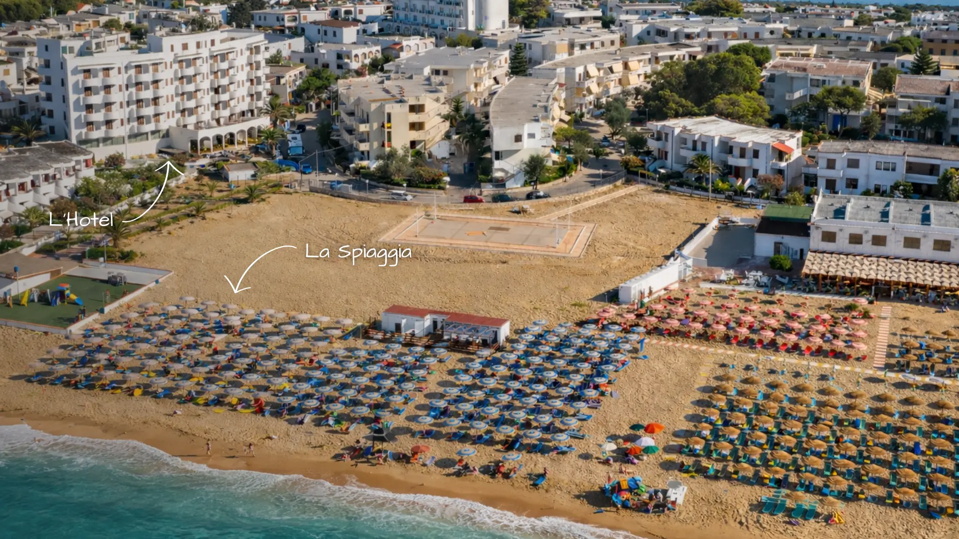 Vista aerea di una spiaggia affollata con ombrelloni e un hotel sullo sfondo.